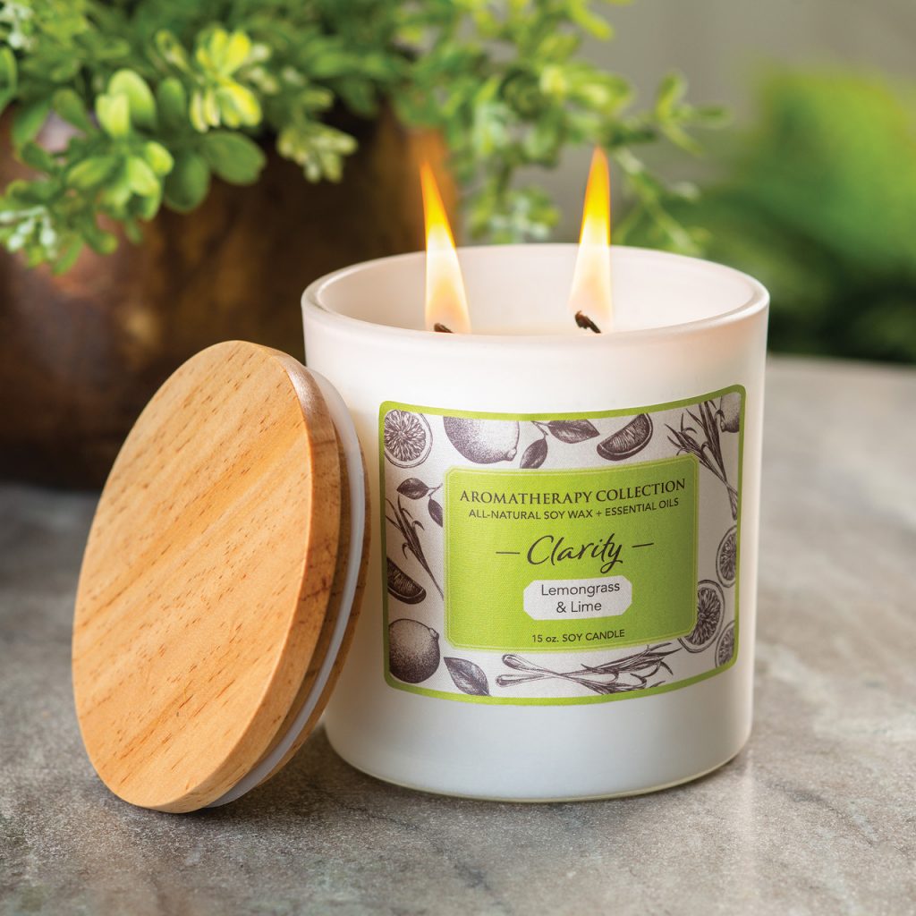 Lit two-wick soy candle in white glass jar with wooden lid, green Aromatherapy Collection Clarity label, Lemongrass & Lime, 15 oz.