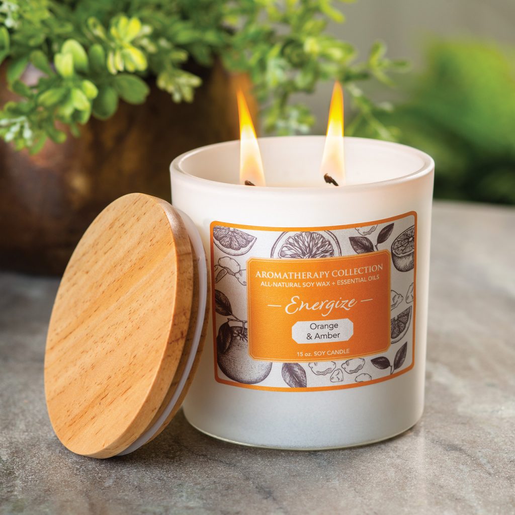 Lit two-wick soy candle in white glass jar with wooden lid, orange Aromatherapy Collection Energize label, Orange & Amber, 15 oz.