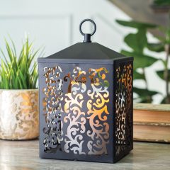 The Cottage Lantern features a scroll-like pattern that casts an ornate glow when lit. The matte metal design comes in a slightly textured, simple black finish.