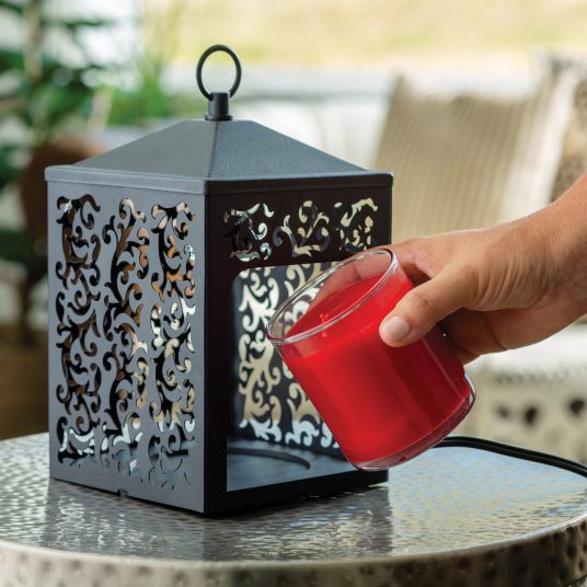 The Cottage Lantern features a scroll-like pattern that casts an ornate glow when lit. The matte metal design comes in a slightly textured, simple black finish.